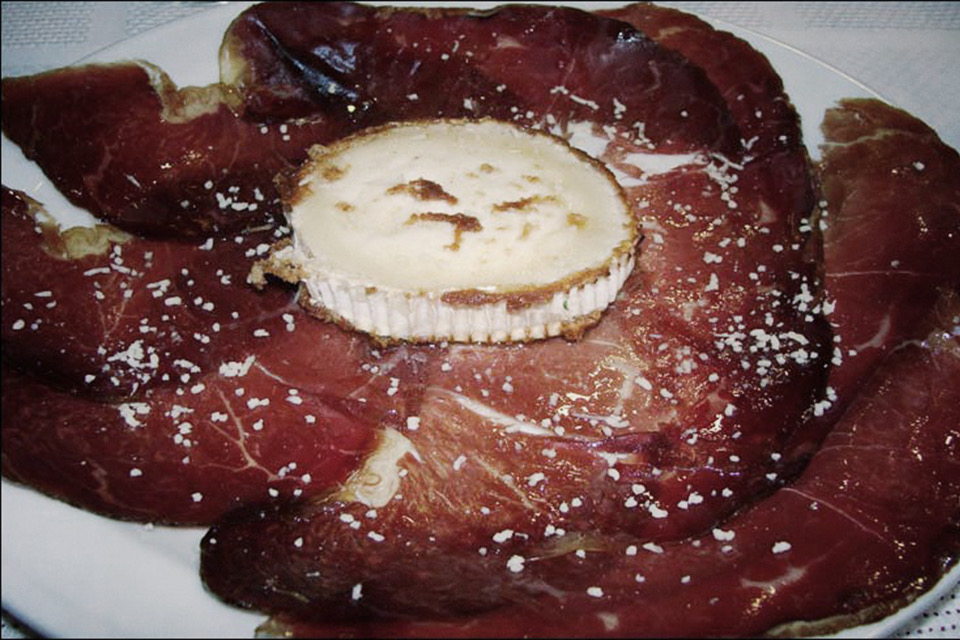 Tabla de jamón con una rodaja de queso de cabra gratinado encima