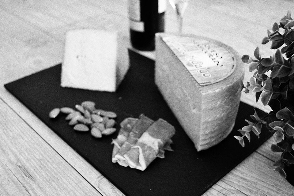 Queso curado en cuña junto a almendras y jamón sobre pizarra