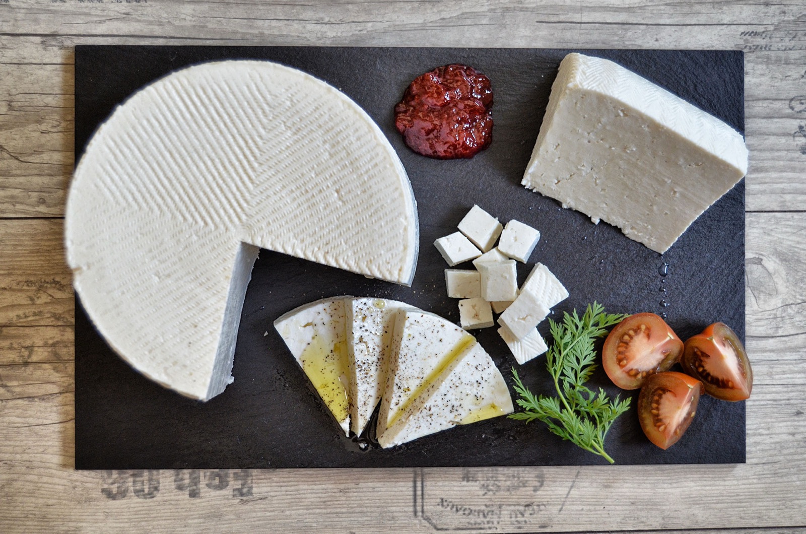 Queso fresco en rueda, en cuñas y en dados sobre pizarra, con tomate y mermelada